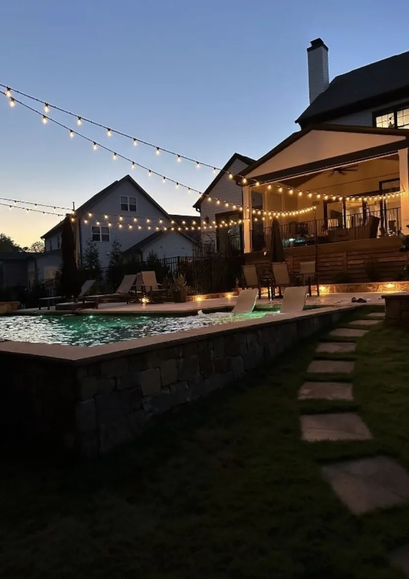 Bistro string lights over a backyard pool and covered patio at dusk